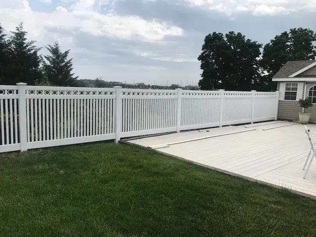 A white fence surrounds a swimming pool in a backyard.