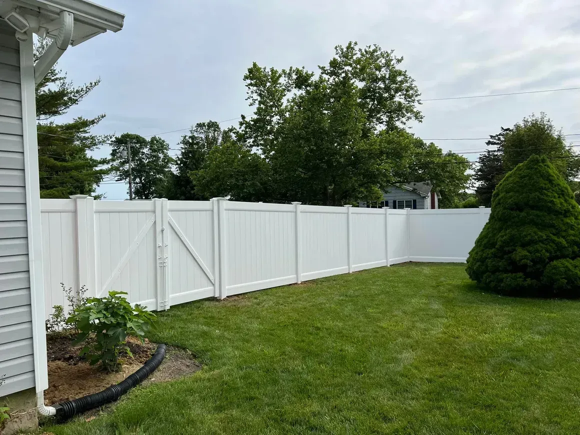 A white fence is in the backyard of a house.
