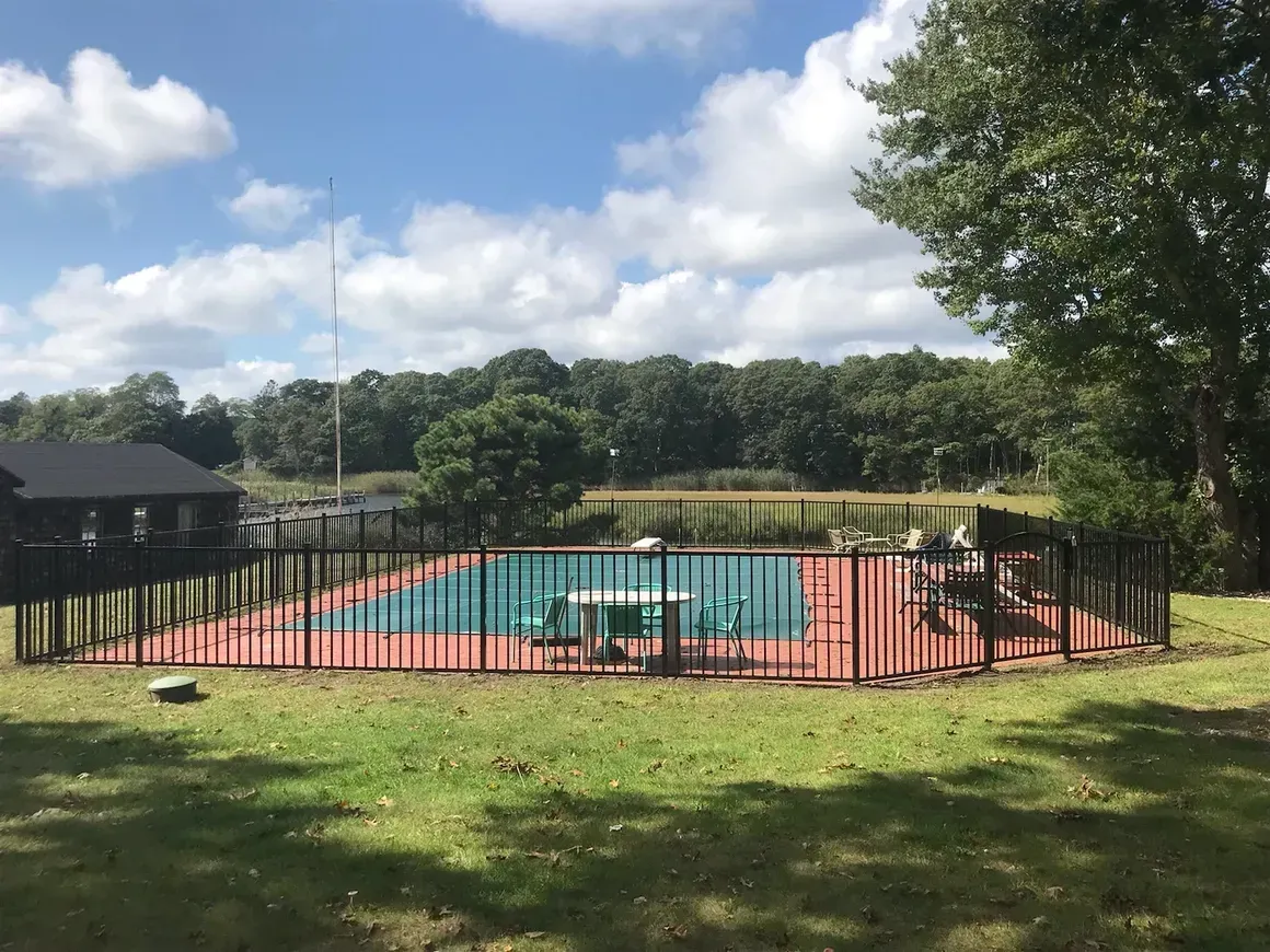 A large swimming pool surrounded by a fence and a picnic table