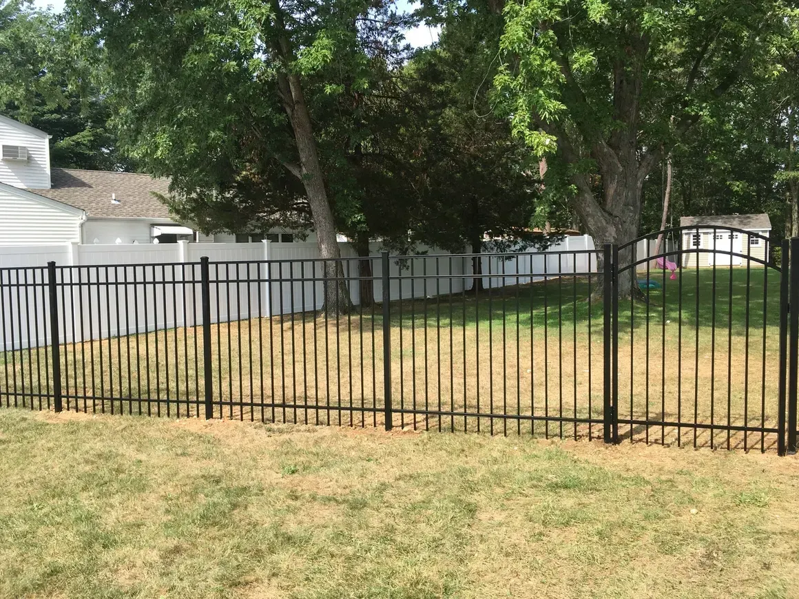 A black metal fence surrounds a grassy yard in front of a house.