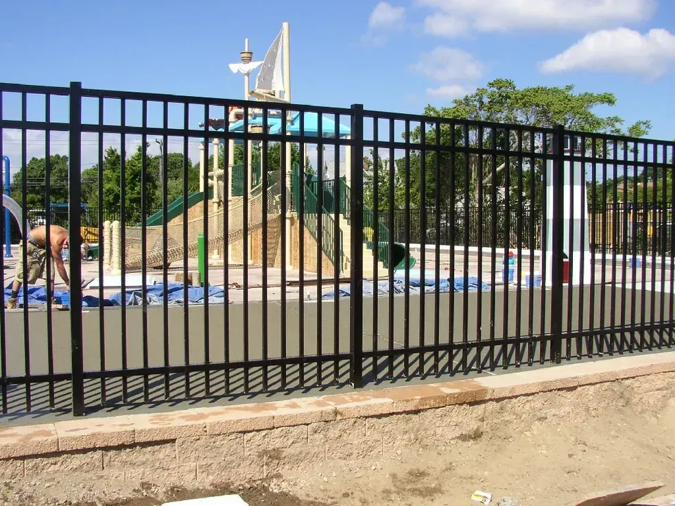 A black metal fence surrounds a playground in a park