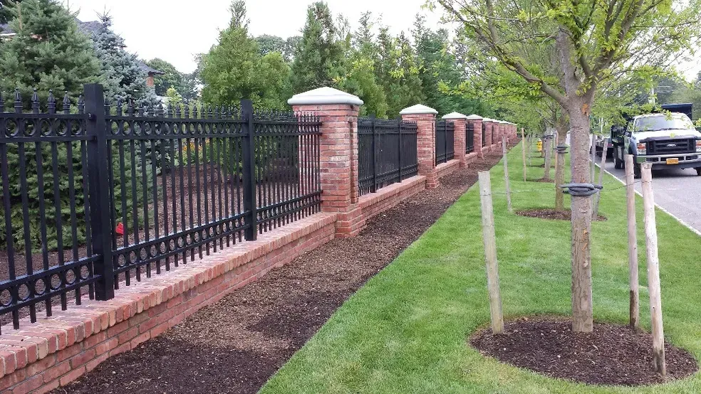 A black fence is surrounded by brick pillars and trees.