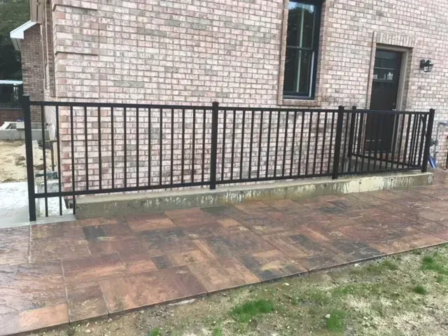 A black metal fence is surrounding a brick house.