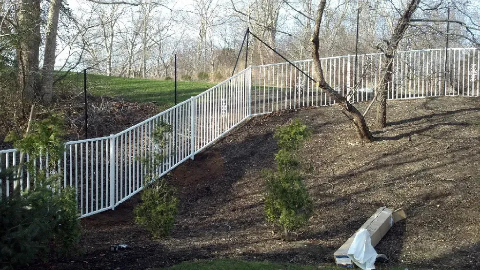 A white fence is sitting on top of a hill surrounded by trees.
