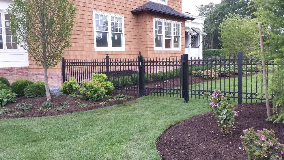 A house with a black fence and a lush green lawn in front of it.