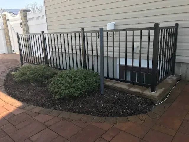 A metal fence is surrounding a basement window of a house.