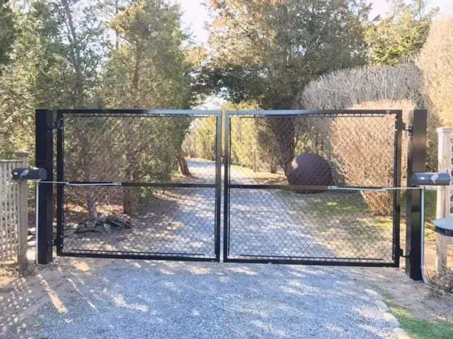 A black gate is sitting on the side of a gravel road.