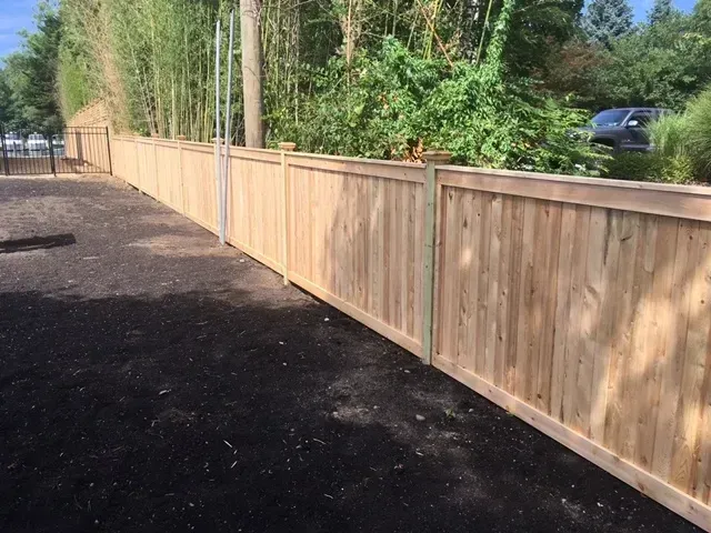 A wooden fence surrounds a parking lot with trees in the background.