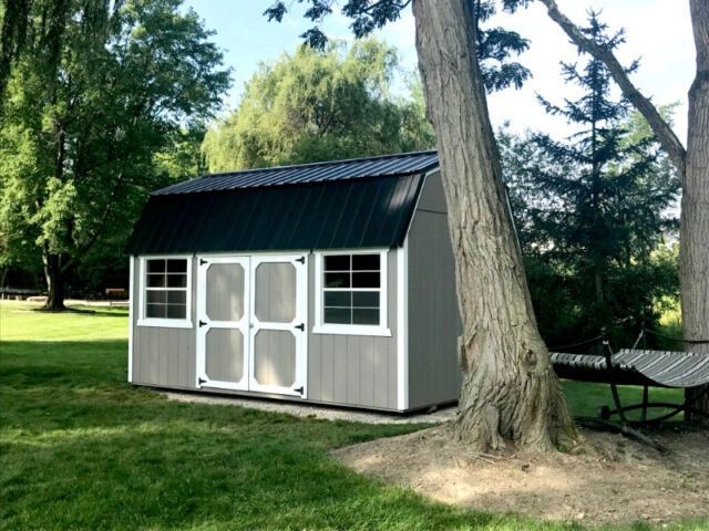 A shed with a black roof is sitting in the middle of a lush green field.