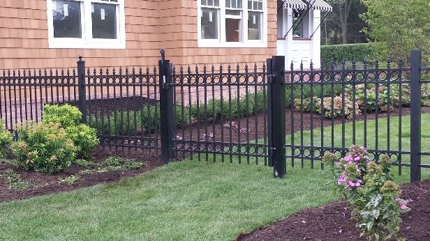 A black fence surrounds a lush green yard in front of a house.