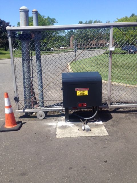 A black box with a yellow sticker on it sits next to a chain link fence