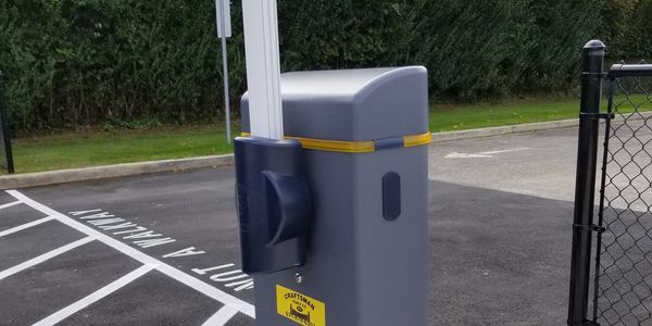 A parking barrier is sitting in a parking lot next to a chain link fence.
