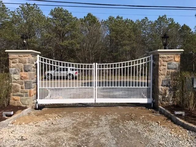 A white gate is surrounded by stone pillars and a car is parked in front of it.