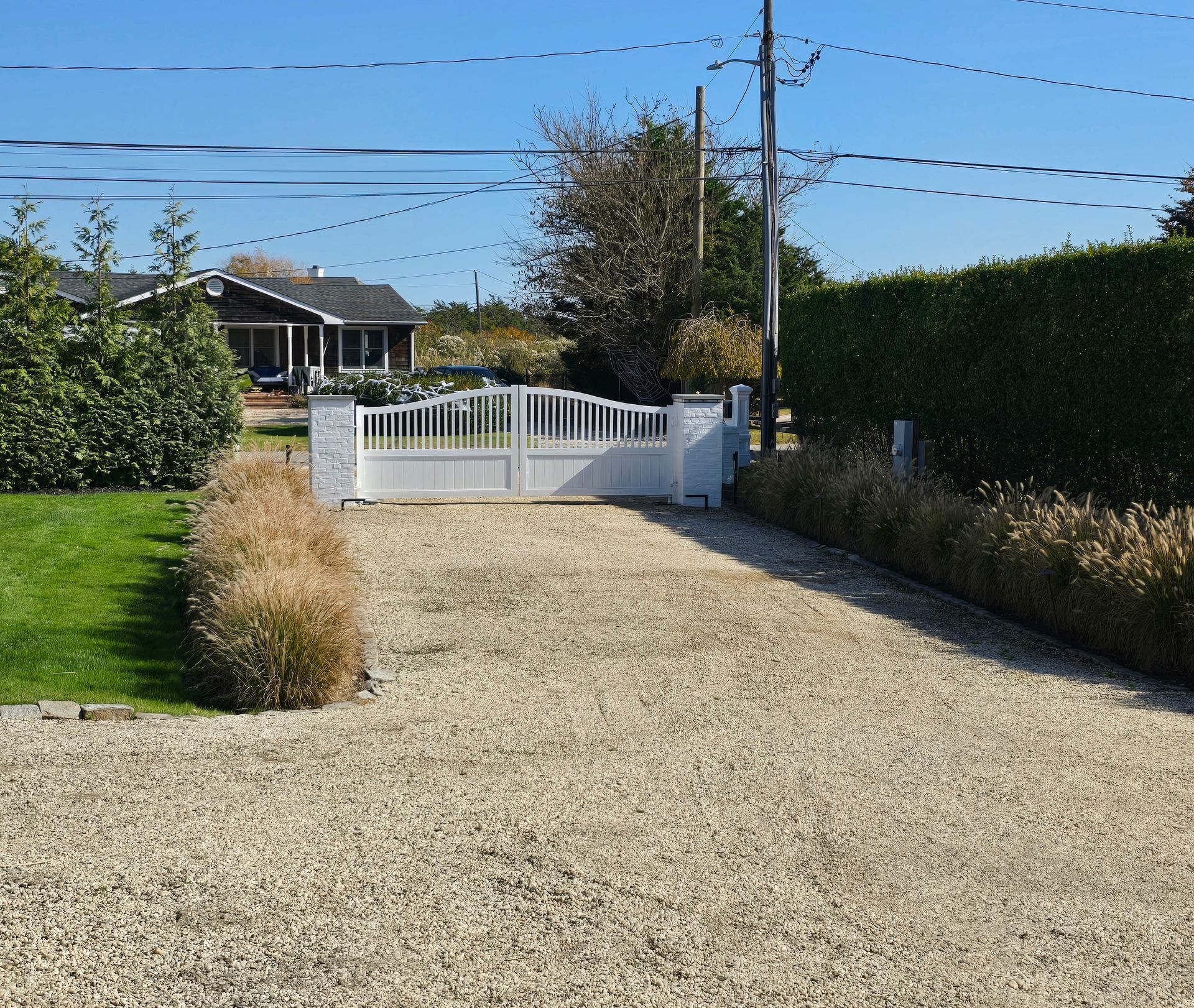 A gravel driveway leading to a house with a white gate