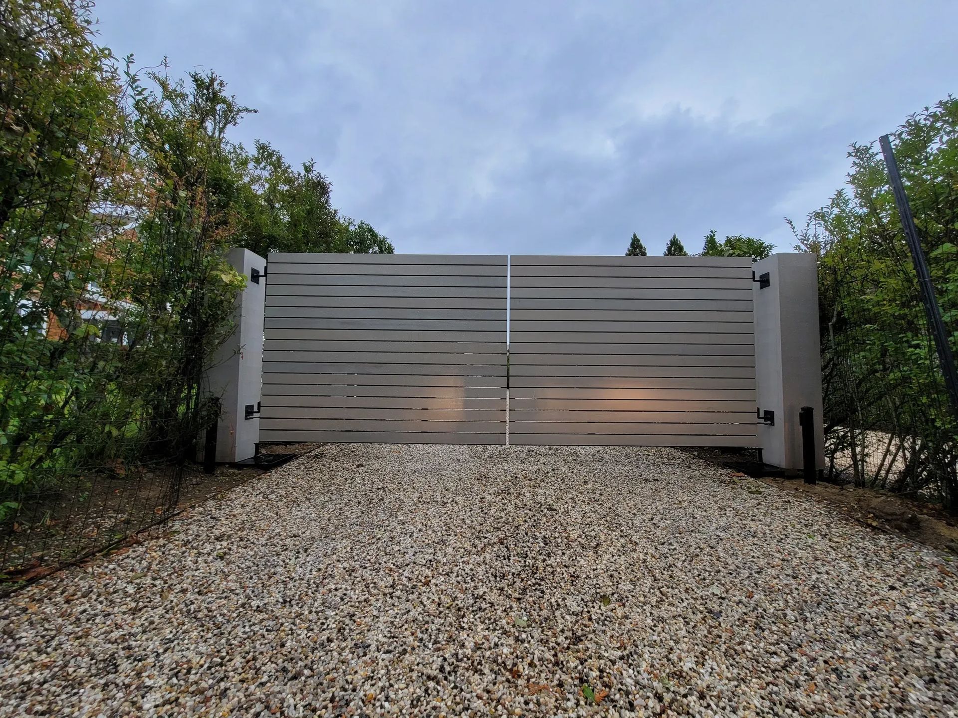 A white gate is open on a gravel driveway