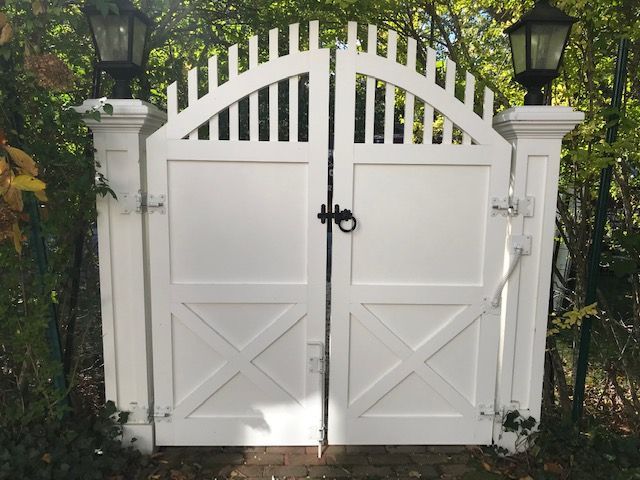 A white gate with a black handle is surrounded by trees and lanterns.