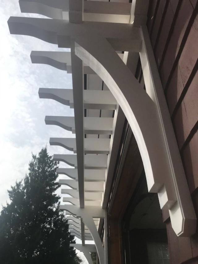 A white pergola is attached to the side of a building.