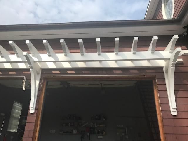 A white pergola is attached to the side of a house.
