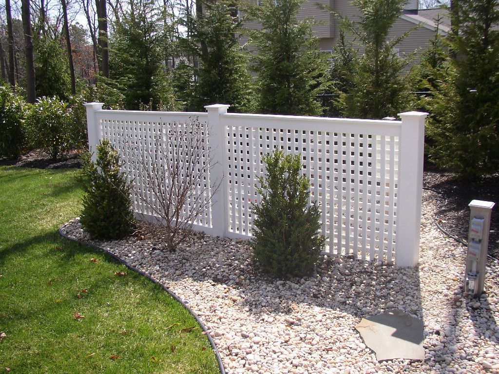 A white fence is surrounded by gravel and trees.