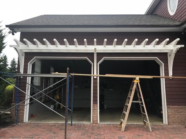 A garage with a pergola and a ladder in front of it.