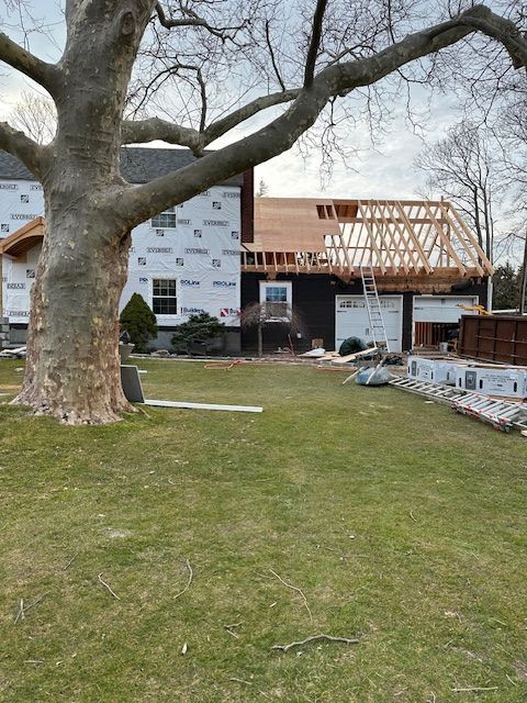 A house is being built in a backyard with a large tree in the foreground.