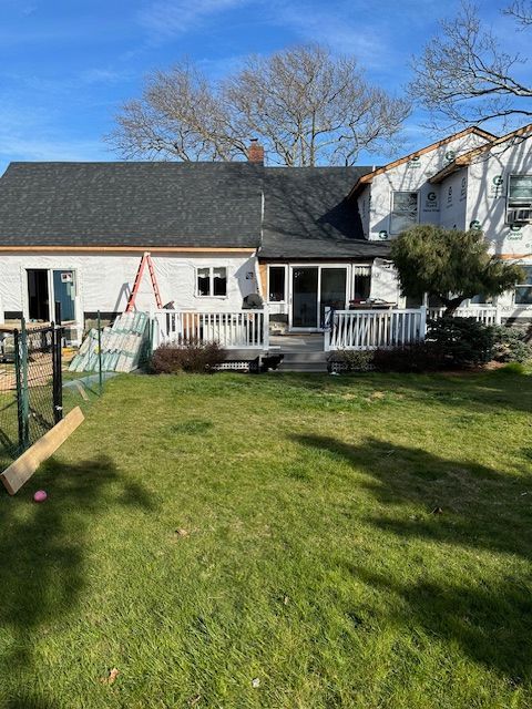 A white house with a black roof is sitting on top of a lush green lawn.