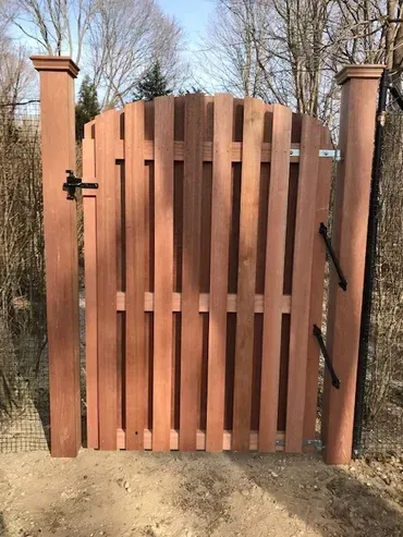 A wooden gate is sitting on top of a gravel driveway in front of a house.
