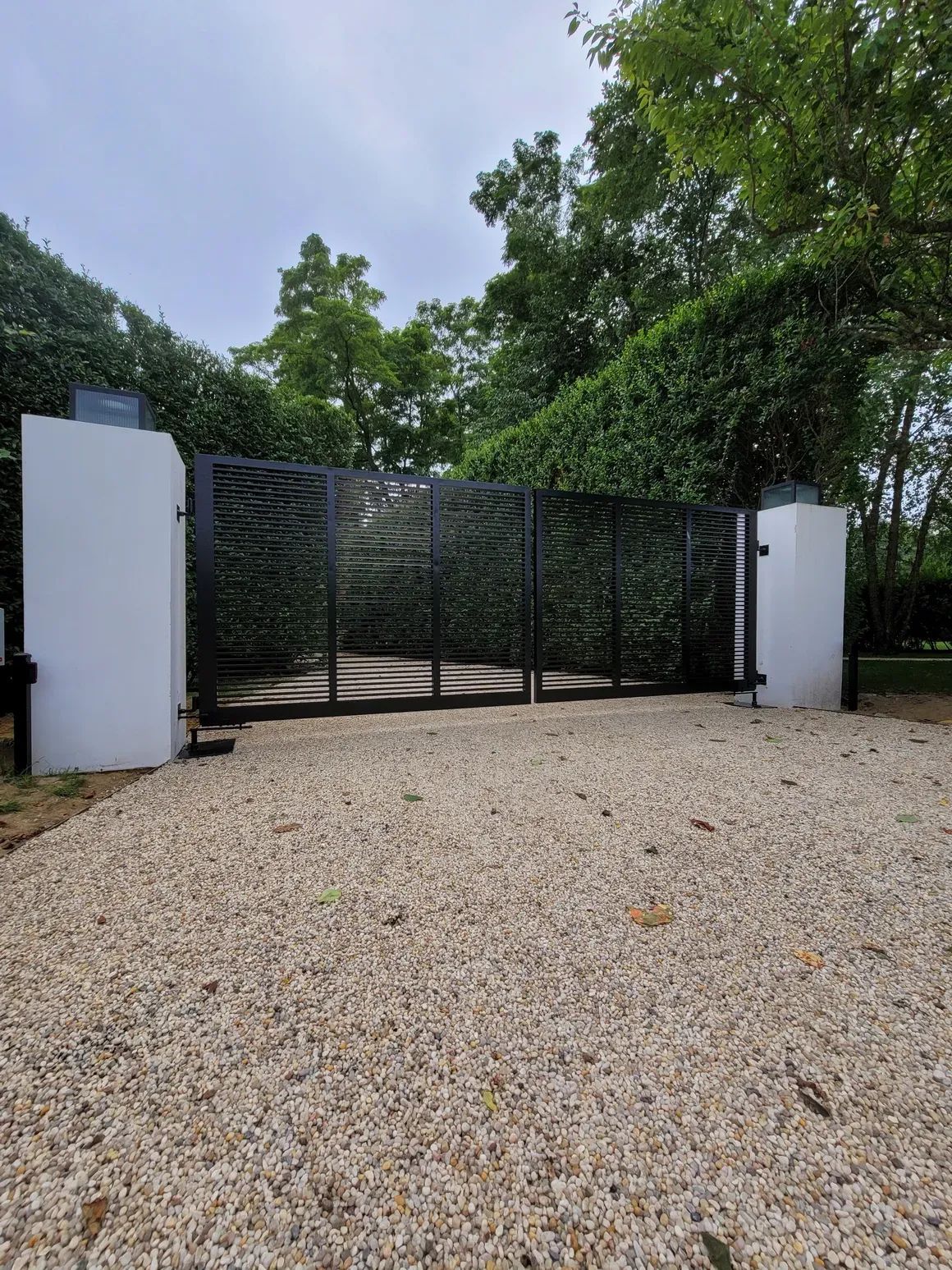 A black gate is sitting in the middle of a gravel driveway.