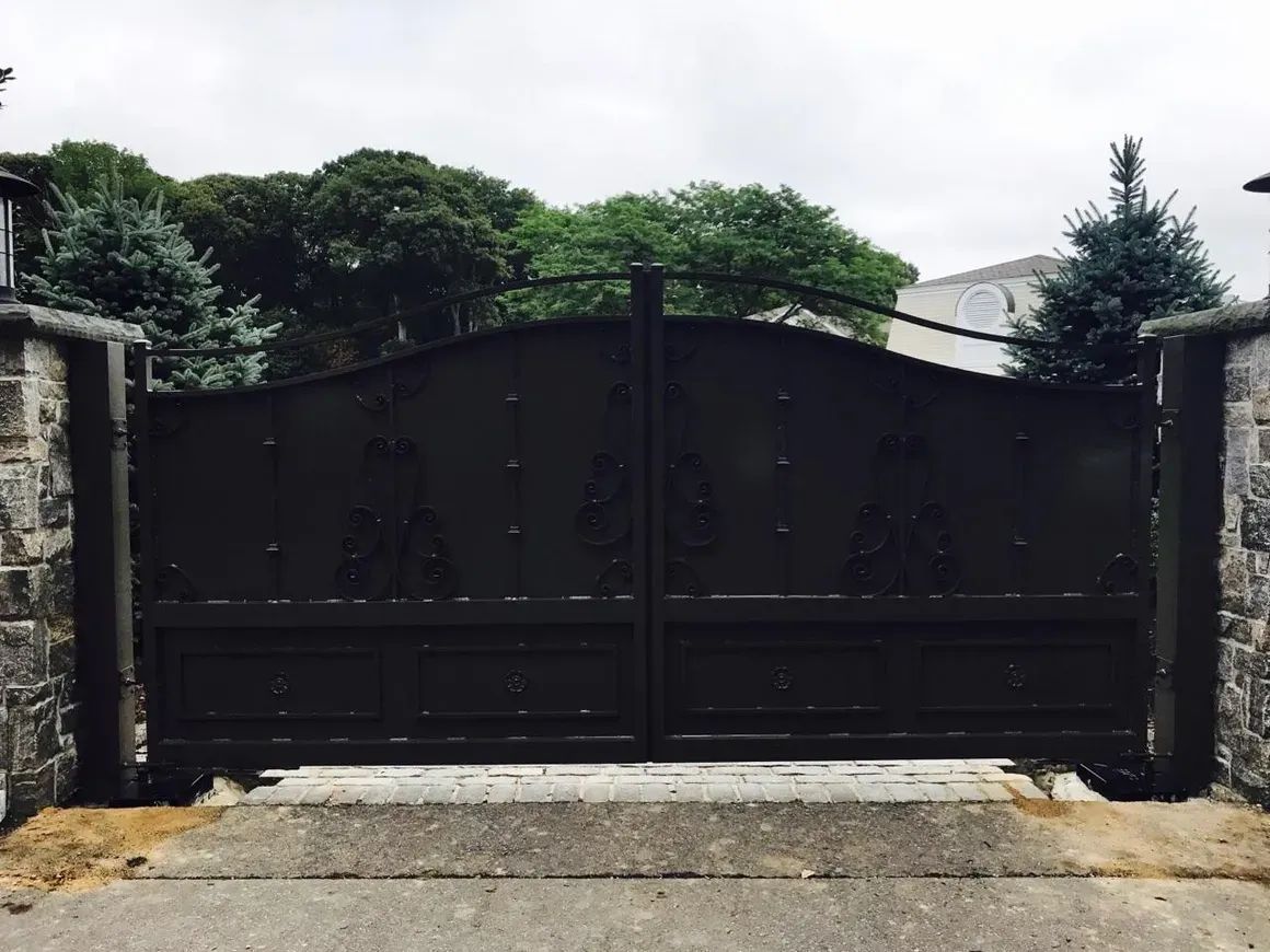 A white gate is surrounded by stone pillars and a car is parked in front of it