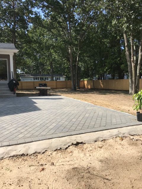 A brick walkway leading to a house with trees in the background.