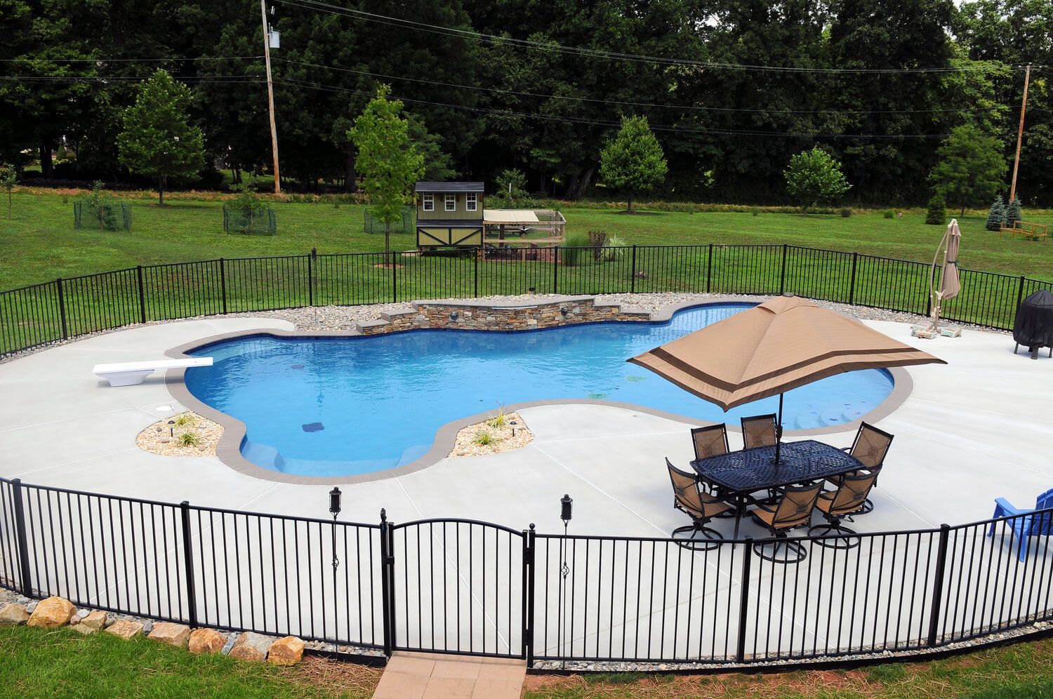 A large swimming pool surrounded by a fence and a table and chairs.