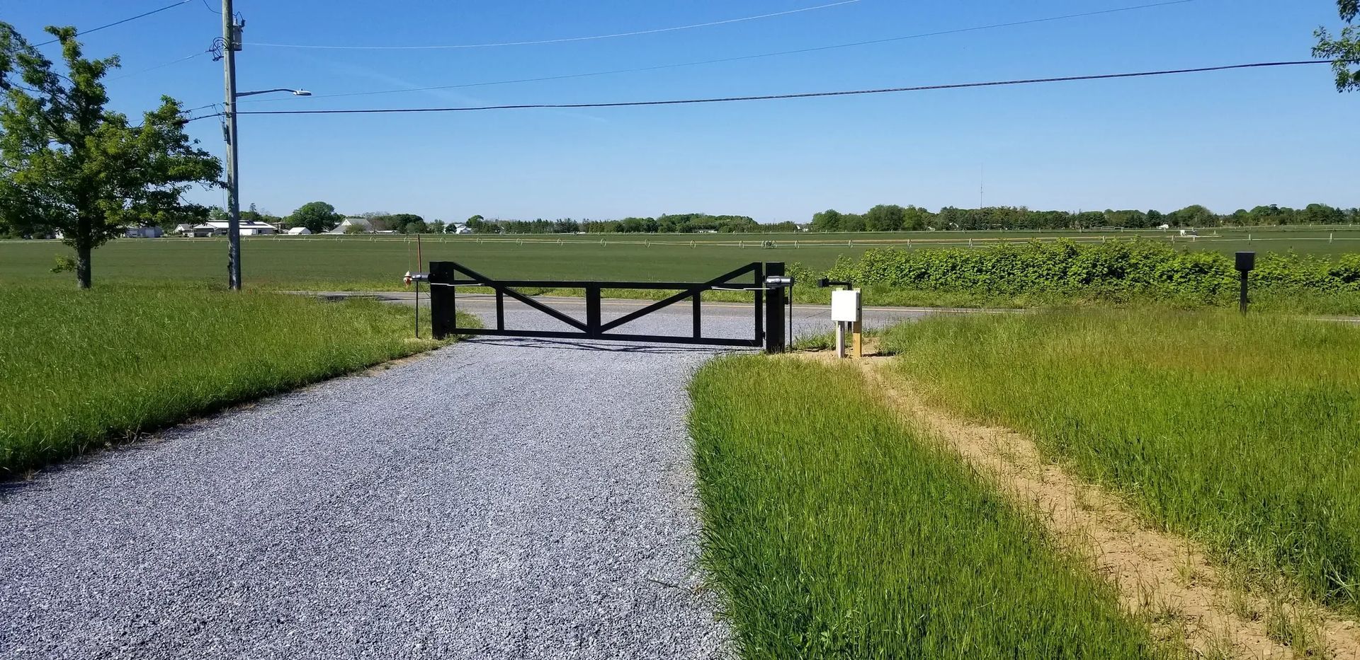 A gravel road leading to a field with a gate