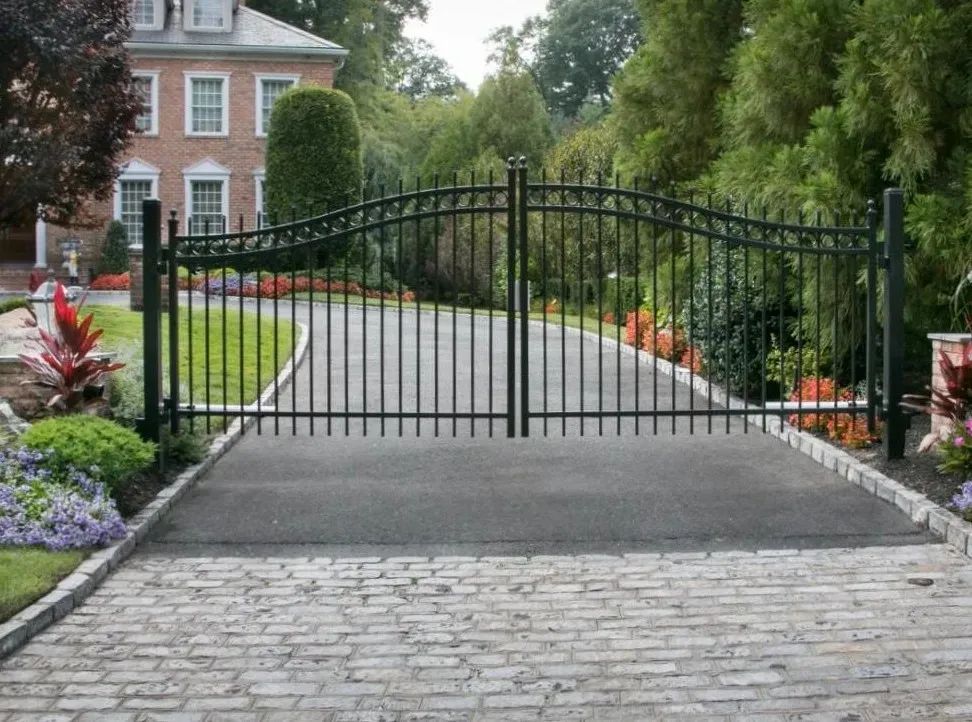 A brick driveway with a wrought iron gate leading to a house