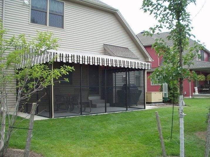 Screened porch attached to a beige house, with striped awning and green lawn.