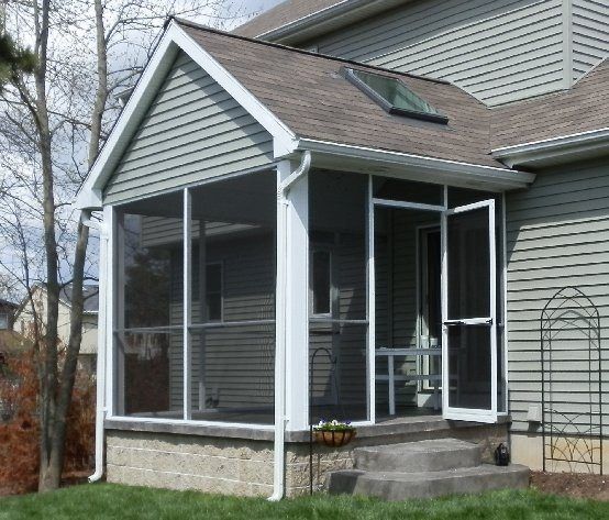 Screened-in porch attached to a house with a gray roof and siding. White trim and screening. Brick base.