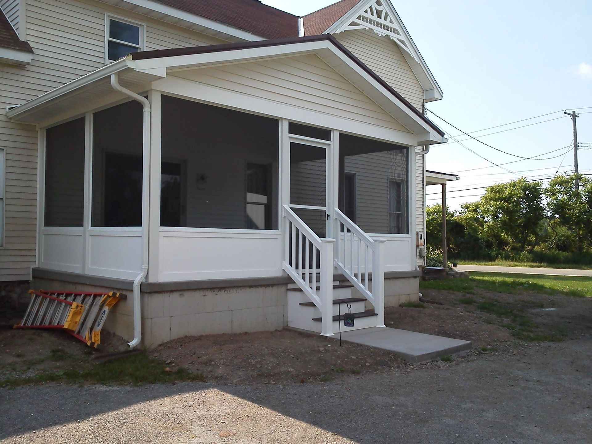 White screened-in porch with steps, attached to a two-story house. A ladder leans against the porch.