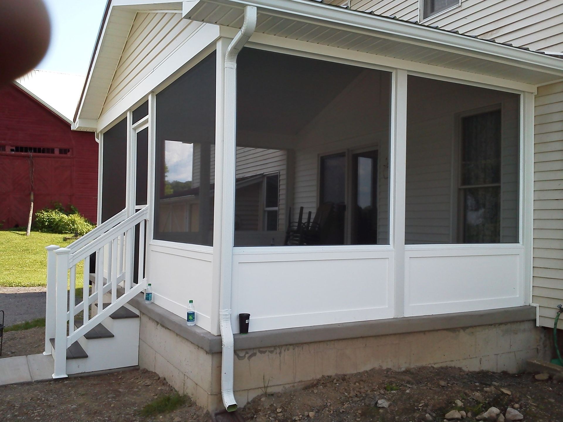 White screened-in porch on a house with a small staircase and a view of a barn.
