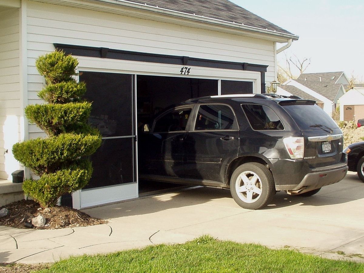 Black SUV partially in a garage with a screen door. A topiary tree is in front.