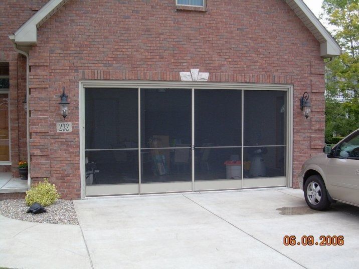Garage with a screened door, beige car parked to the right, brick exterior.