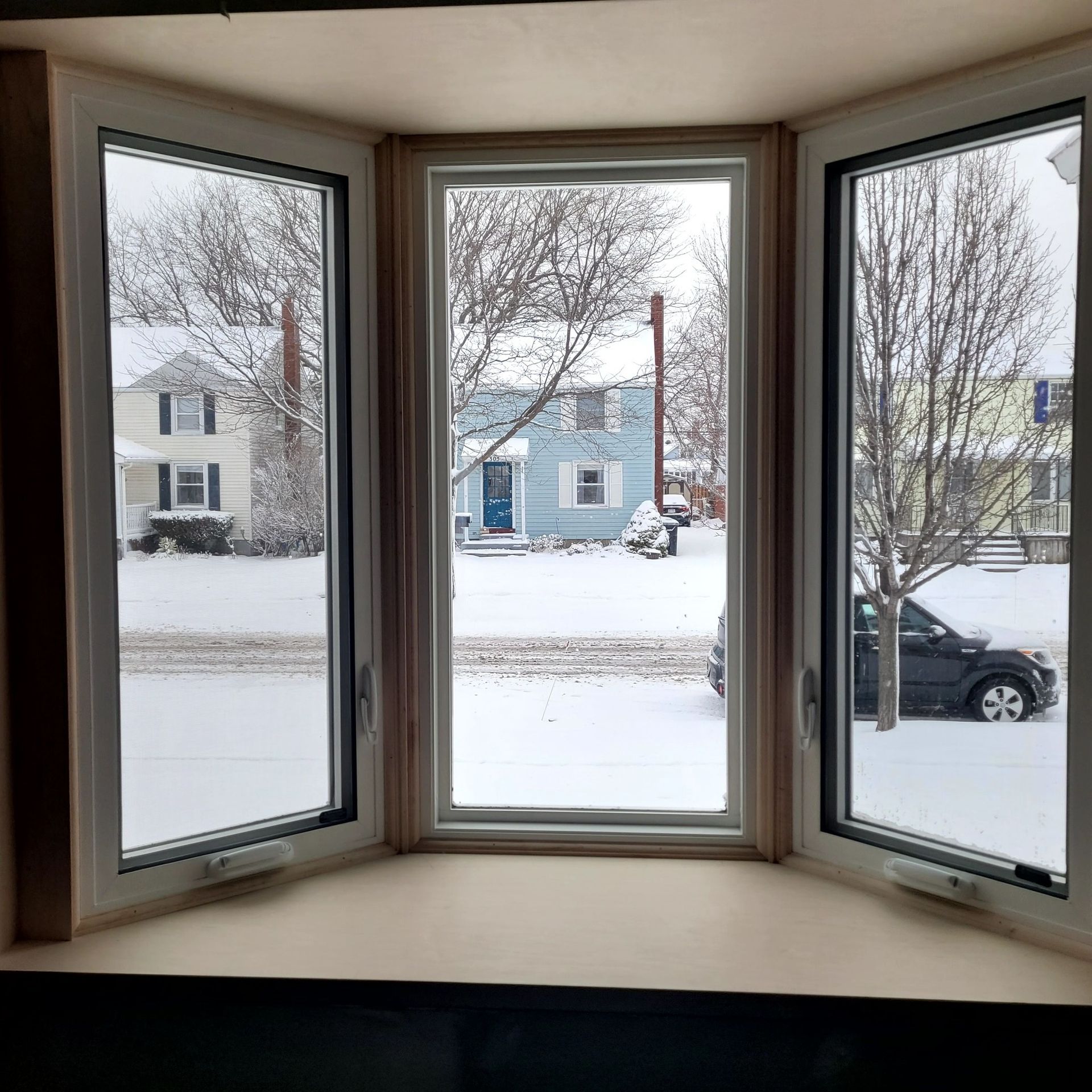 Bay window overlooking a snow-covered street and houses.