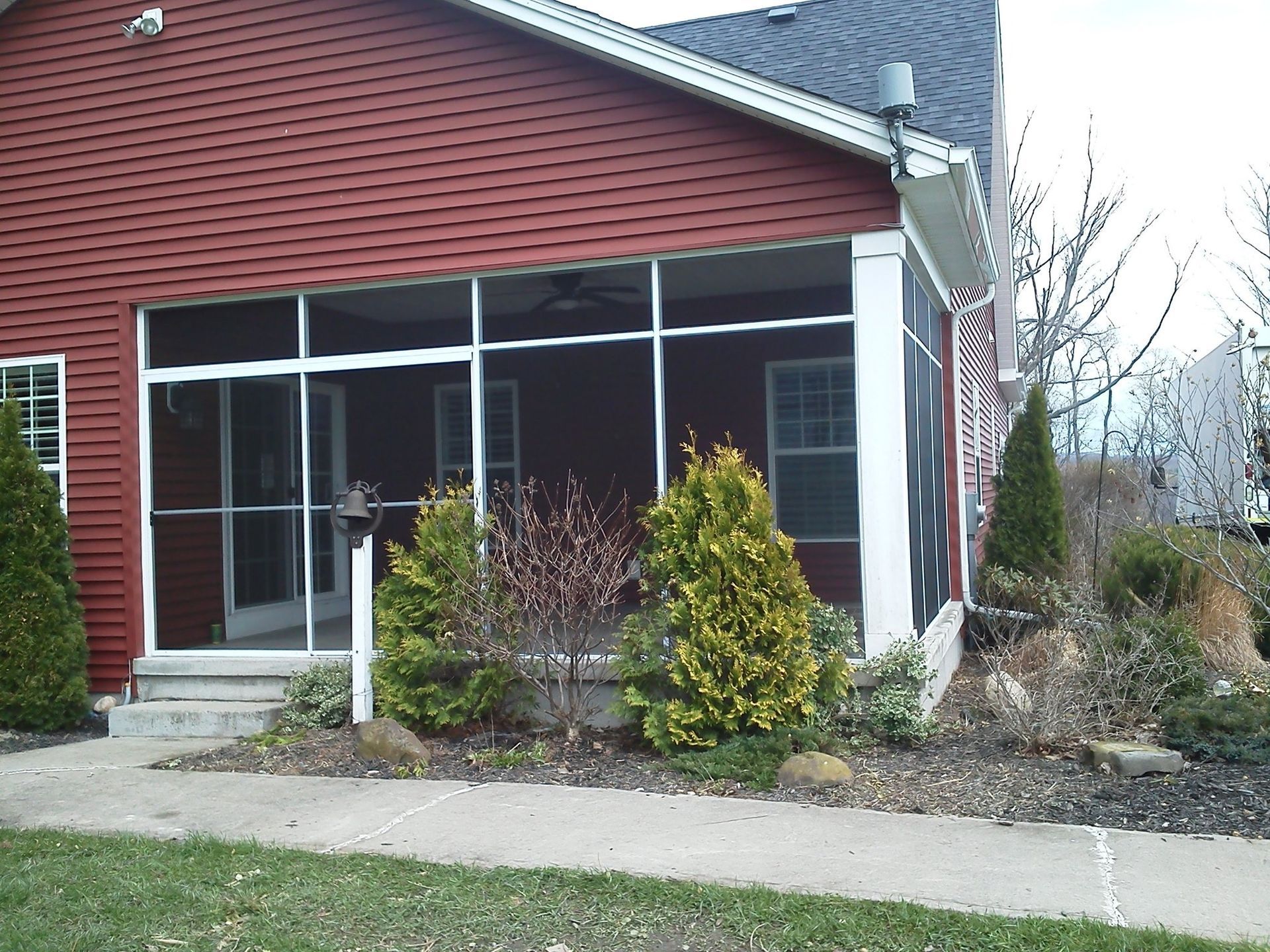 Red house with a screened-in porch, landscaping in front.