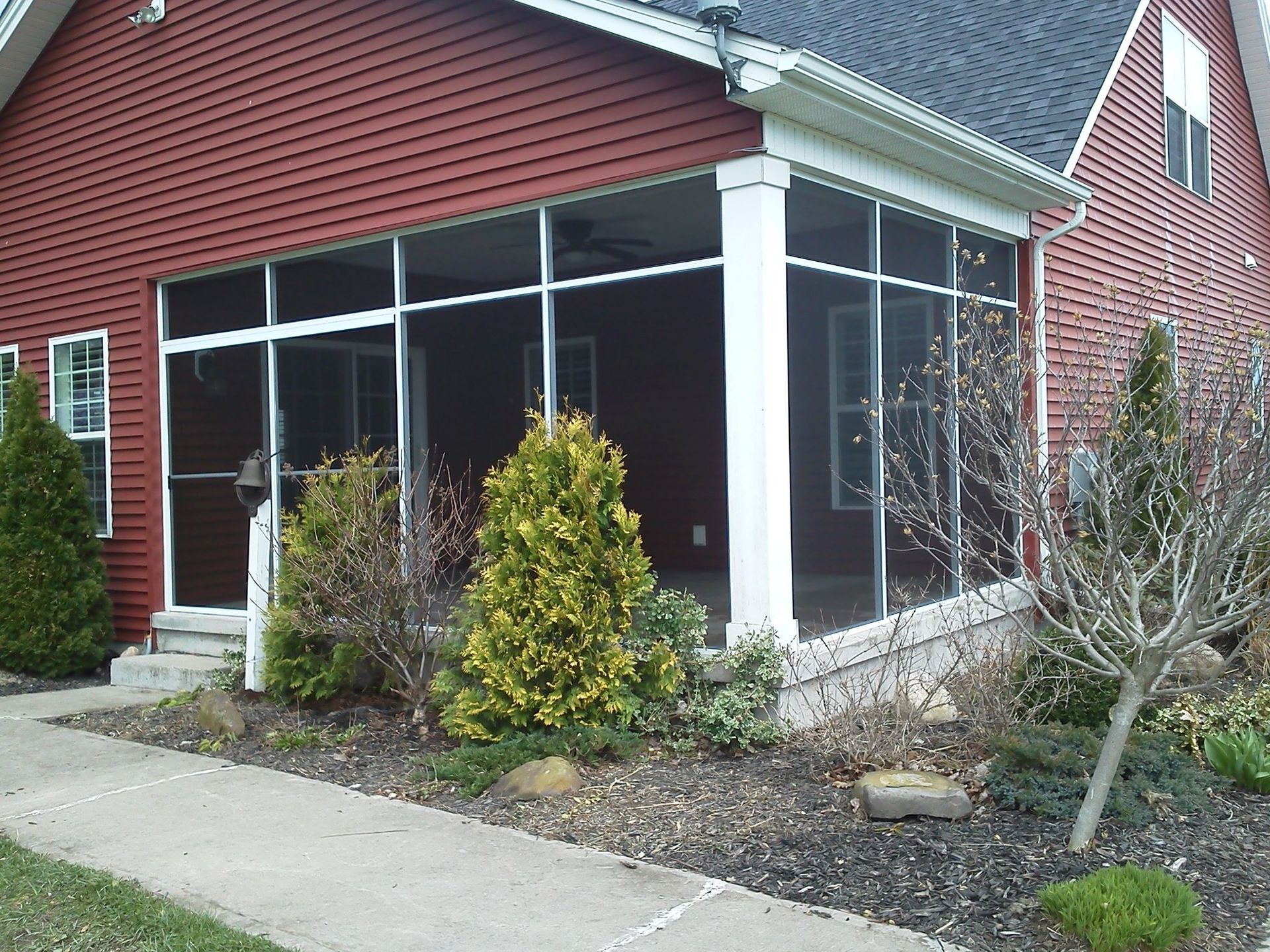 Red house with screened porch, white trim, and landscaping along a walkway.