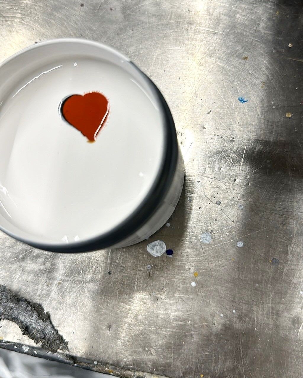 White container with red heart-shaped opening, filled with white liquid, on a metal surface.