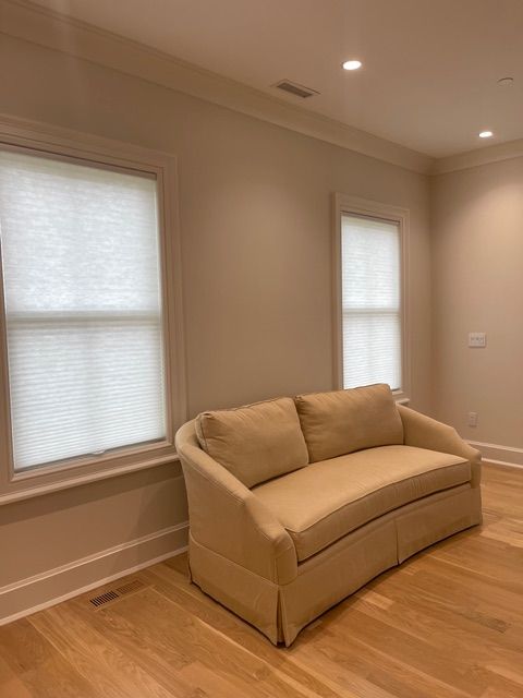 Beige sofa in a room with wood floors, two windows with blinds, and recessed lighting.