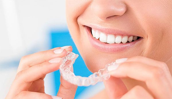 Woman holding a clear aligner, smiling, showing straight teeth.