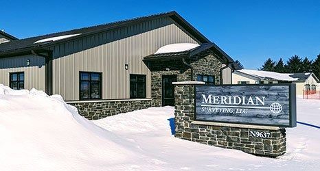 A Meridian Manufacturing building in a snowy landscape with a stone and metal exterior and a branded front sign.