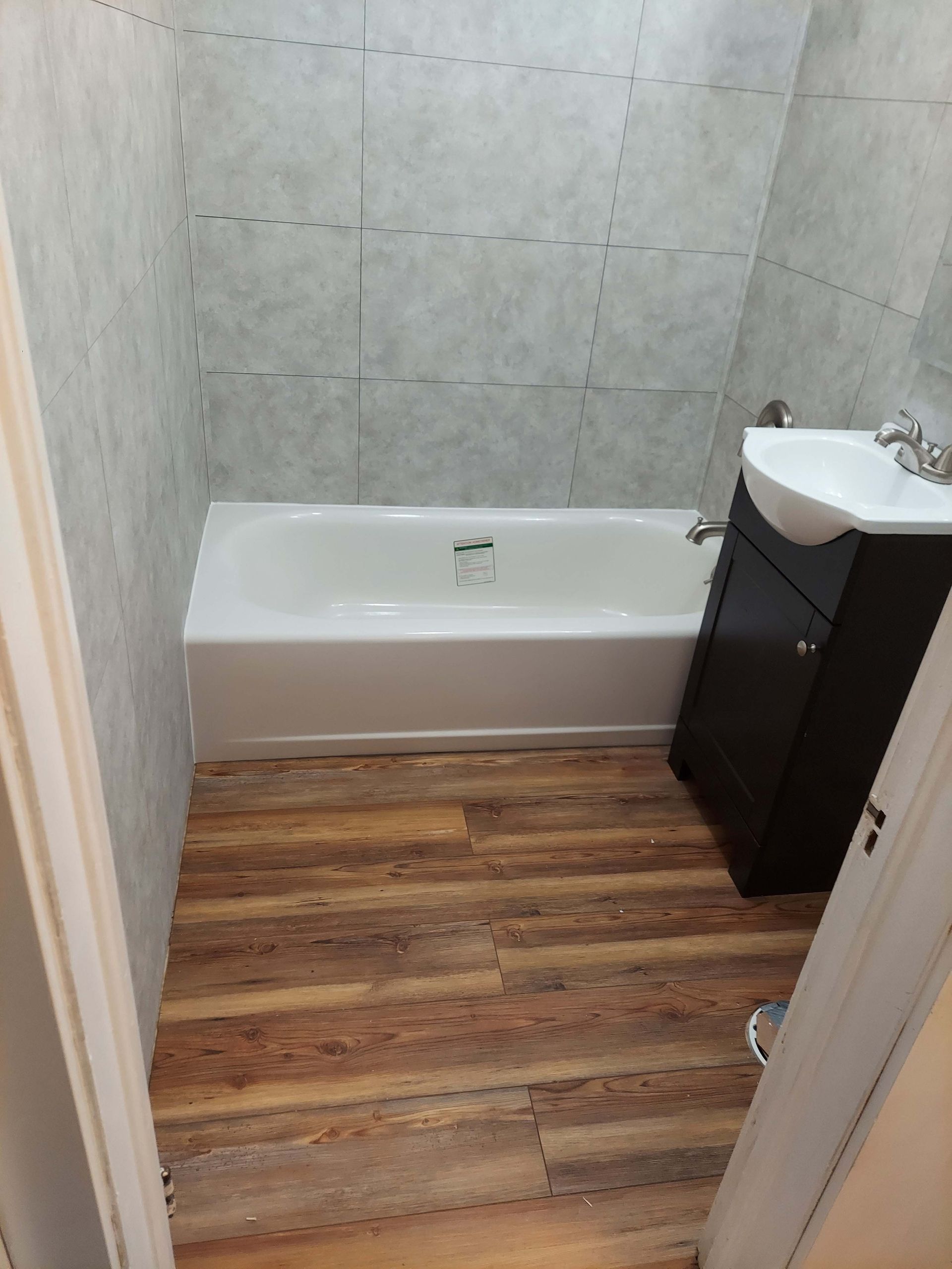 A bathroom with a bathtub , sink , and wooden floor.