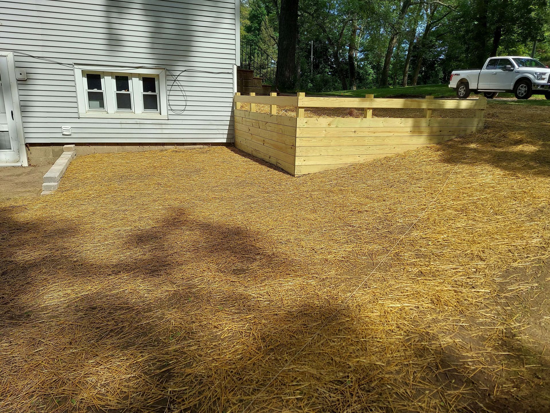 A white truck is parked in front of a house with a wooden fence.