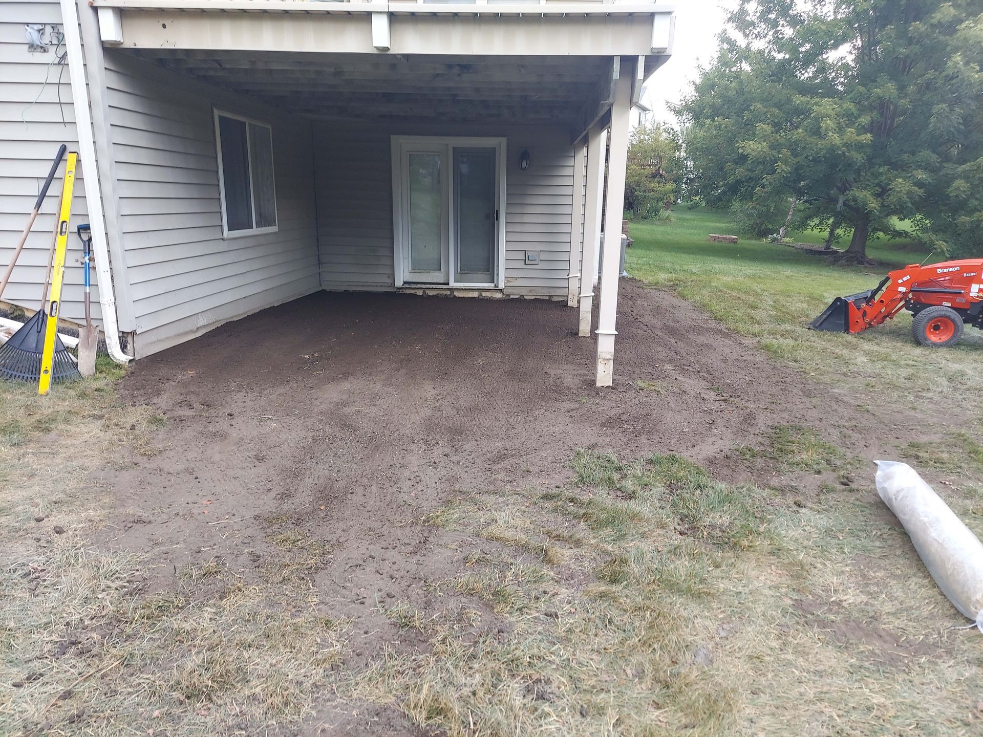 A tractor is parked in front of a house with a covered patio.