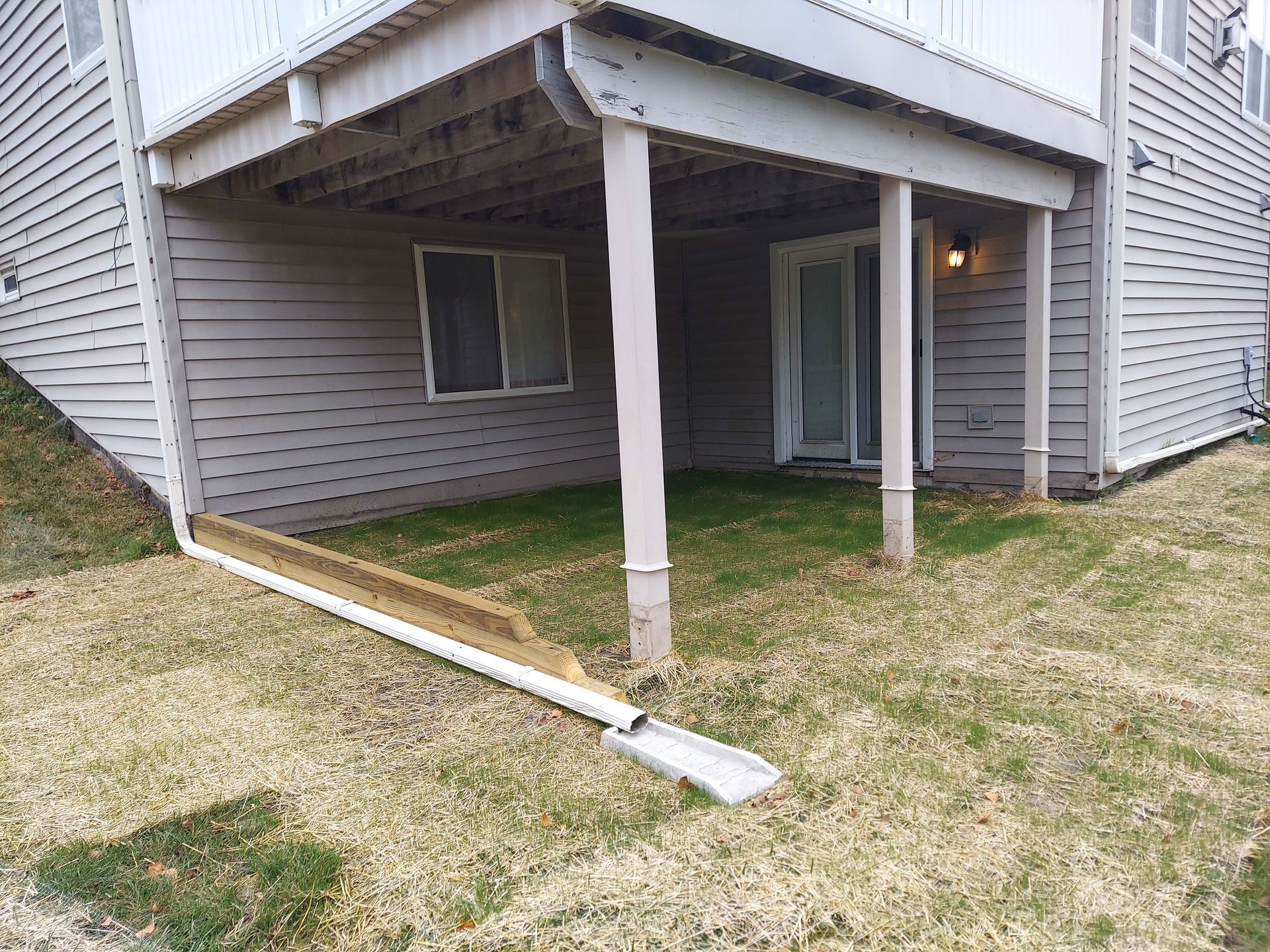 A house with a covered patio and a drain pipe in the grass.
